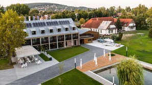 A modern building with a rooftop garden, outdoor seating area, and a small boat dock. - Alsóörs Marina Hotel (Alsoors)