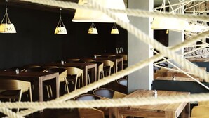 A restaurant with wooden tables and chairs, hanging pendant lights labeled 'M-3', and a rope barrier. - Alsóörs Marina Hotel (Alsoors)