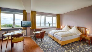 Una camera d'albergo con un letto, una televisione, un tavolo con sedie e vista sul mare.