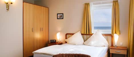 Habitación de hotel con cama, mesitas de noche, armario y vista al mar.