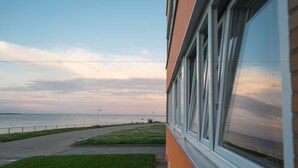 Vista sulla costa da un edificio con un'area verde antistante e un vialetto lastricato che conduce al mare.