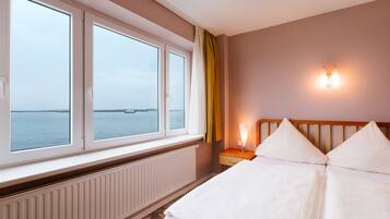 Une chambre d’hôtel comprenant un lit, une table de chevet avec une lampe, une fenêtre avec des rideaux et un luminaire fixé au mur.