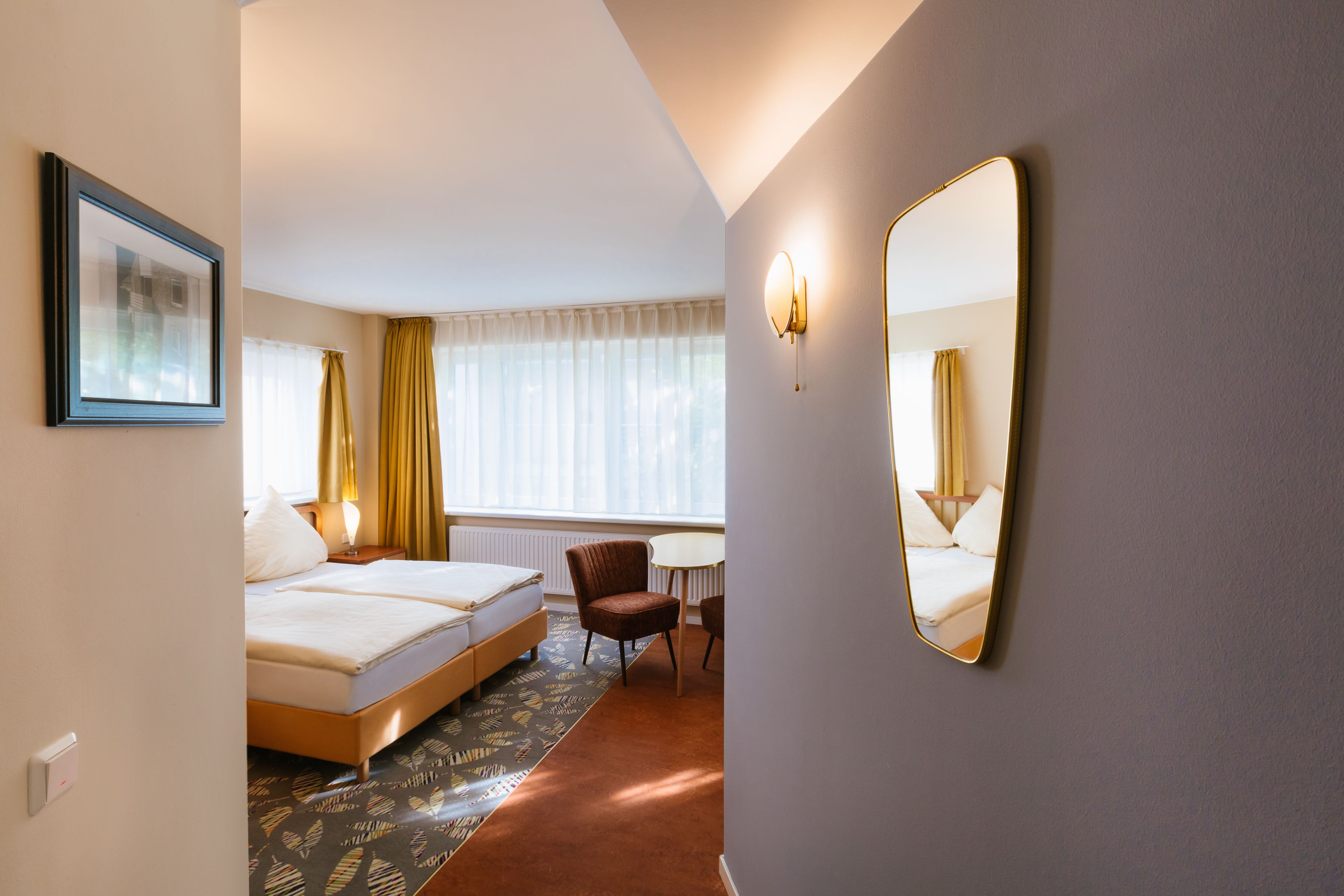 A hotel room with a bed, a chair, a desk, and a large mirror.