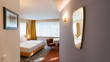 A hotel room with a bed, a chair, a desk, and a large mirror.