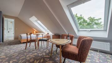 A room with a bed, a round table with chairs, a skylight, and a patterned carpet.