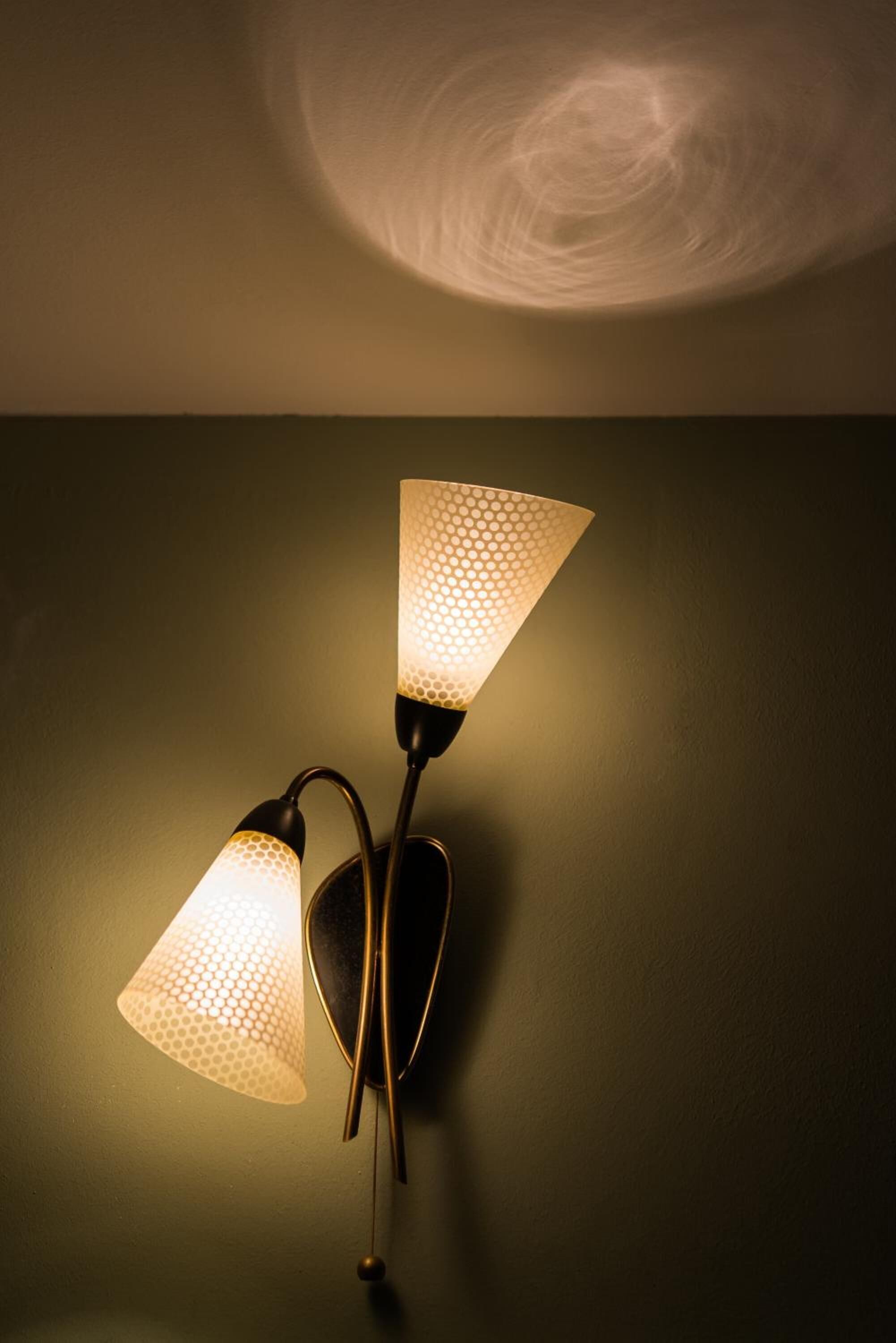 A wall-mounted lamp with two conical shades against a plain wall.
