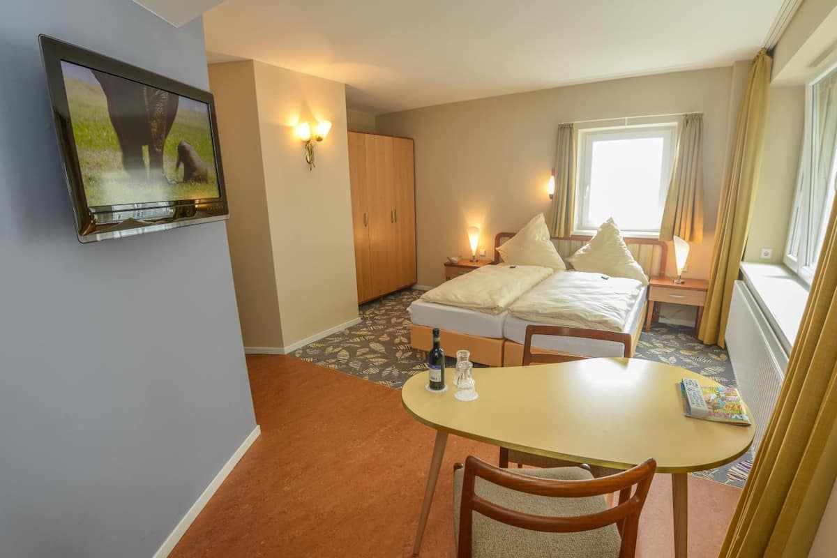 Una habitación de hotel con cama, televisor montado en la pared, una mesita con un control remoto y una ventana con cortinas.