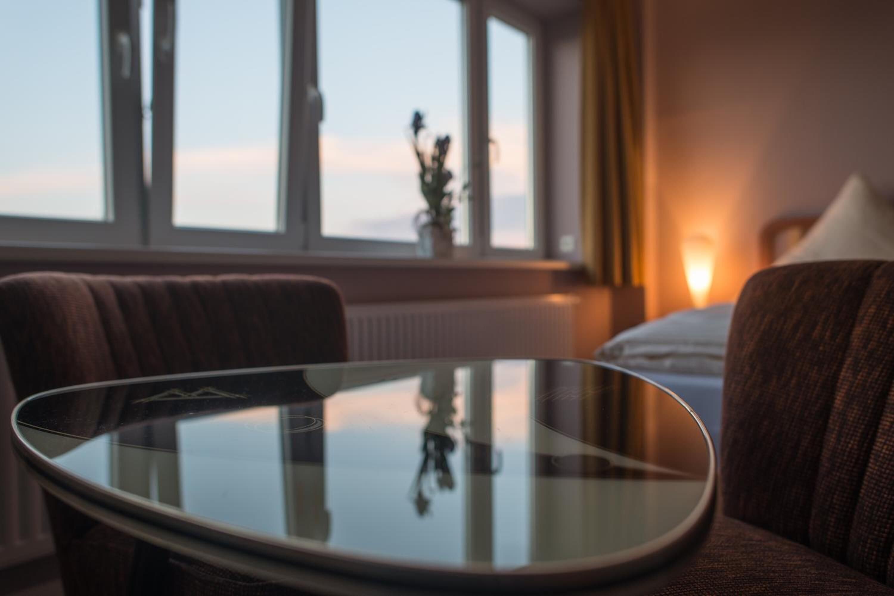 Hotelkamer met een glazen tafel, een bank, een bed en een raam met uitzicht op de lucht.