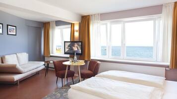 A hotel room with a bed, a sofa, a small table with a TV, and a view of the sea.