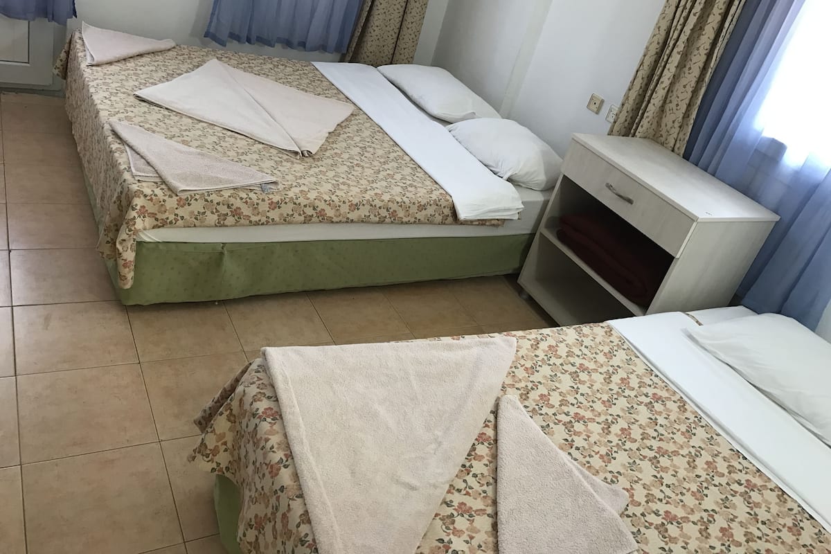 Habitació amb dos llits, cadascun amb roba de llit floral i almoades blanques, una taula de nit petita i un armari.