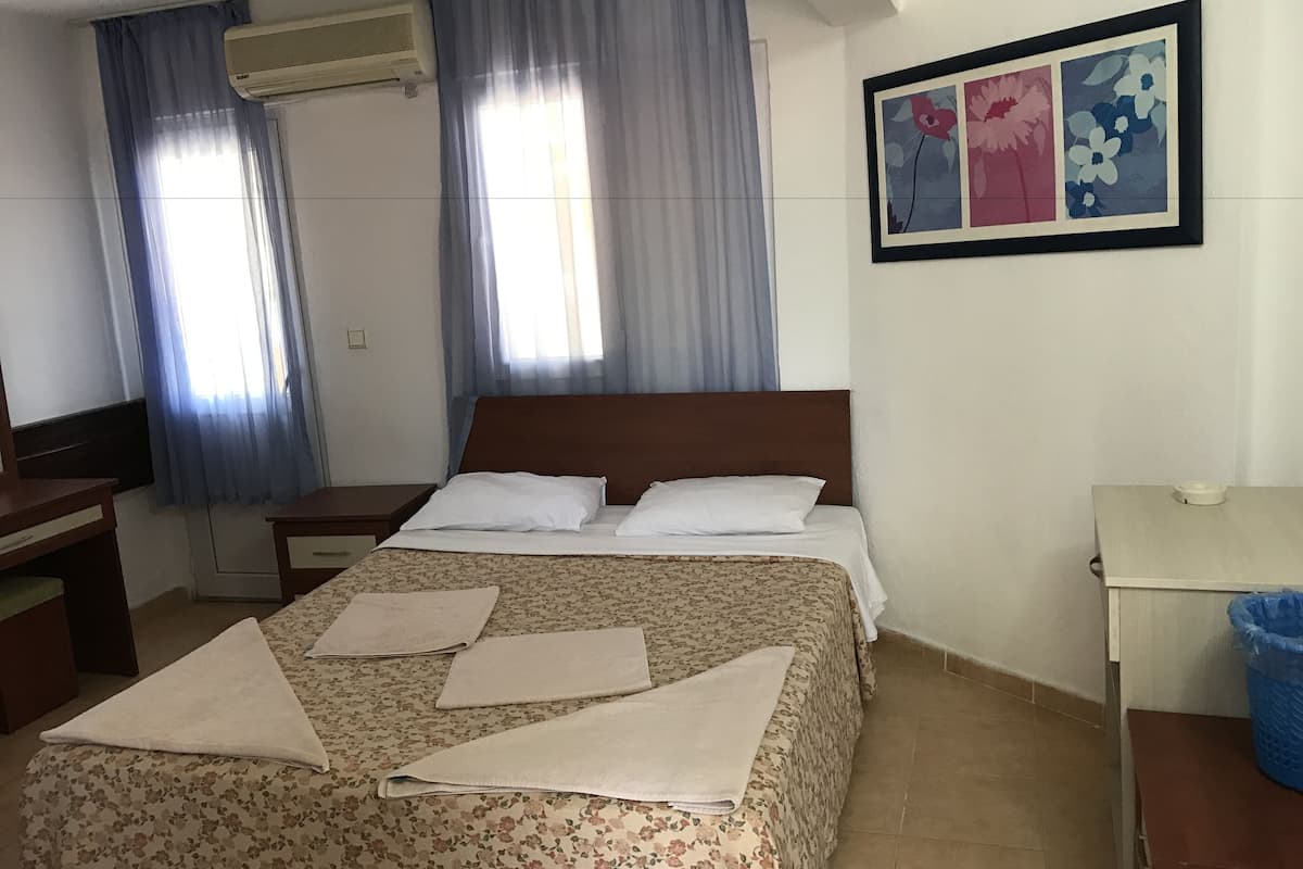 Una habitació d'hotel amb un llit, una taula de treball, una cadira, un safata de paper blau i una obra d'art floral emmarcada a la paret.