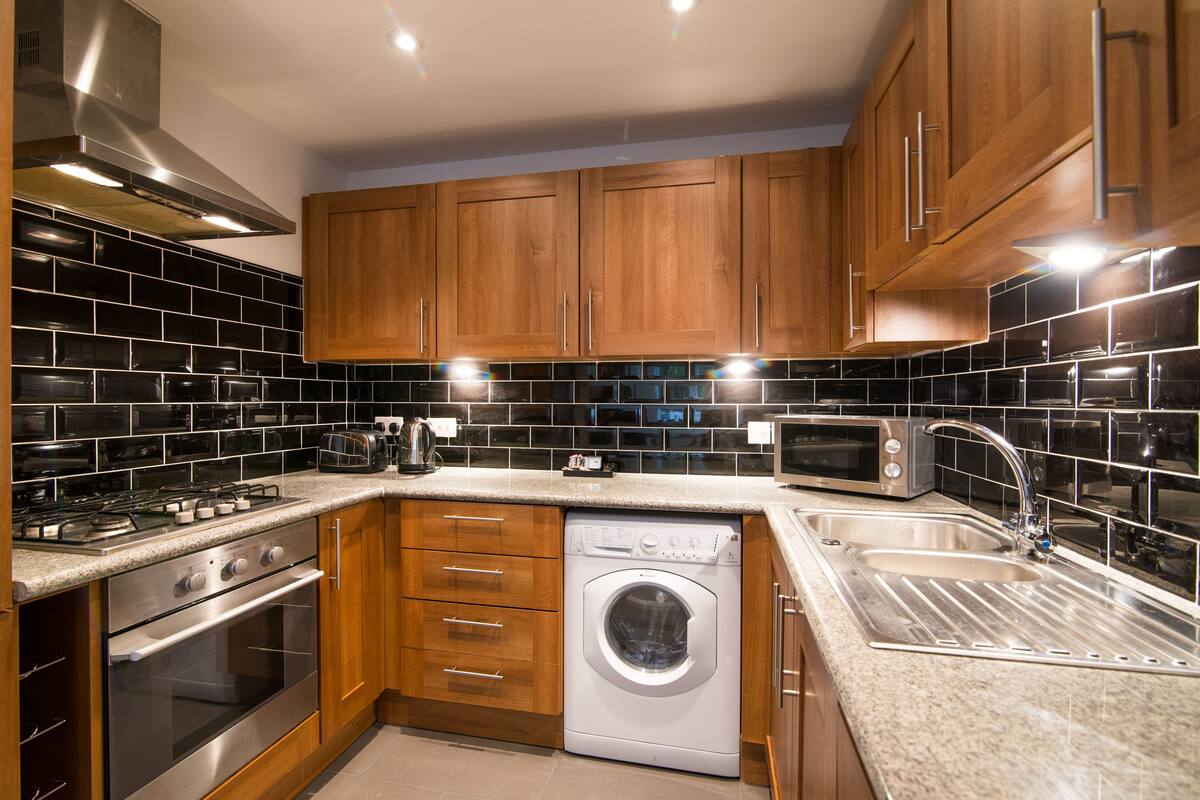 A modern kitchen with wooden cabinets, a stainless steel range, a built-in oven, a microwave, a dishwasher, and a double sink.