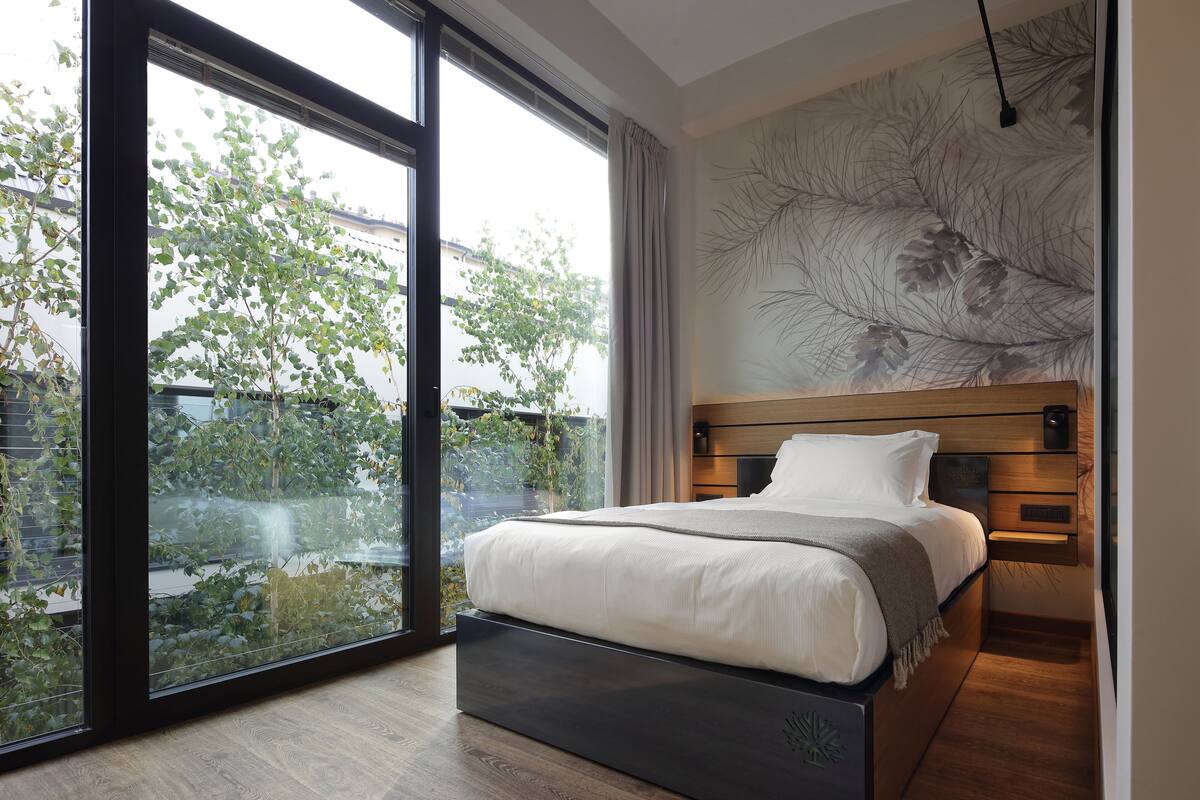 A modern bedroom with a large window, a bed with a wooden headboard, and a wall-mounted artwork.