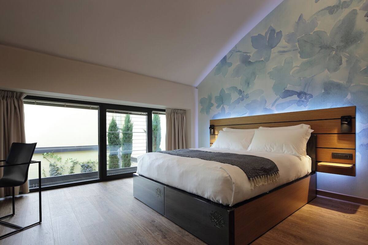 A modern bedroom with a large bed, a view of greenery through a sliding door, and a floral wall mural.