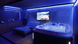 A modern spa room with a hot tub, a massage table, and a TV screen displaying a beach scene. - Versoverde Alzaia Naviglio Grande (Milan)
