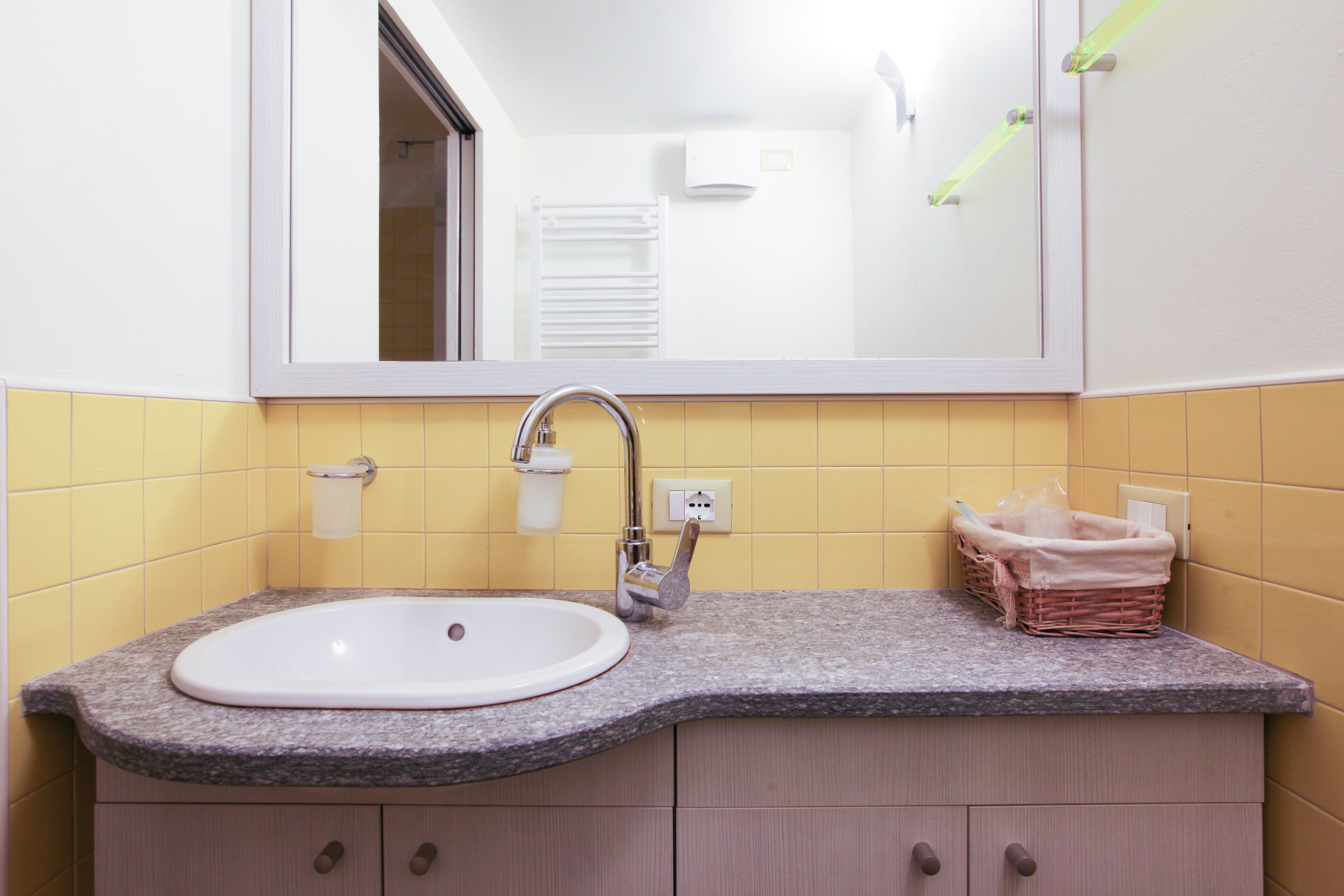 Un baño con un lavamanos blanco, un espejo y una pared con azulejos amarillos.