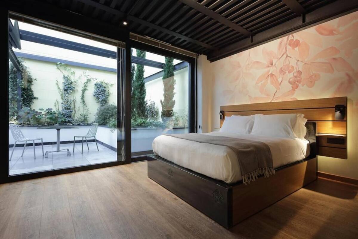 A modern bedroom with a large bed, a glass door leading to a balcony, and a floral wall mural.