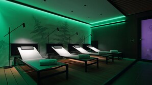 A room with four reclining chairs, each with a pillow and a small table. The room has a green ambient lighting and a wooden floor. - Versoverde Alzaia Naviglio Grande (Milan)