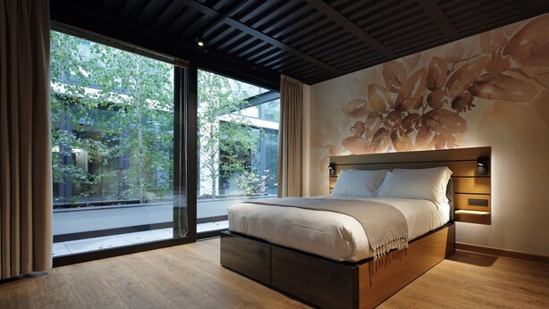 A modern bedroom with a large bed, a view of greenery outside, and a wooden ceiling. - Versoverde Alzaia Naviglio Grande (Milan)