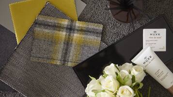 A black surface with a Nuxe skincare product, a bouquet of white roses, and a yellow and gray plaid fabric.
