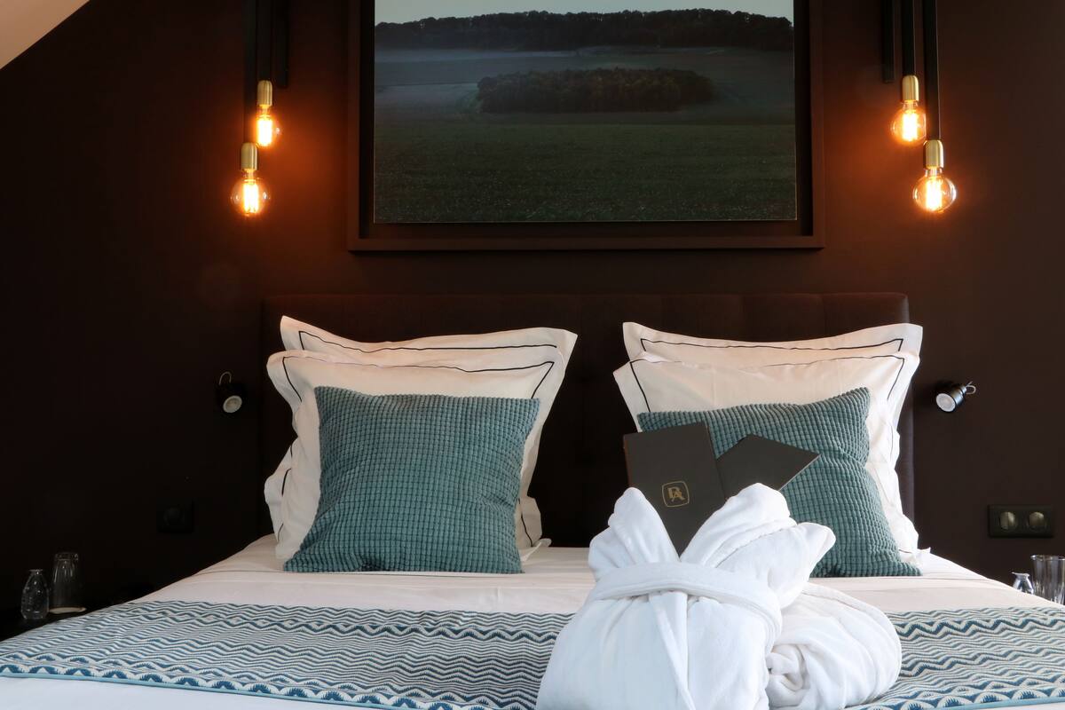A hotel room with a bed, pillows, a robe, and a framed picture on the wall.