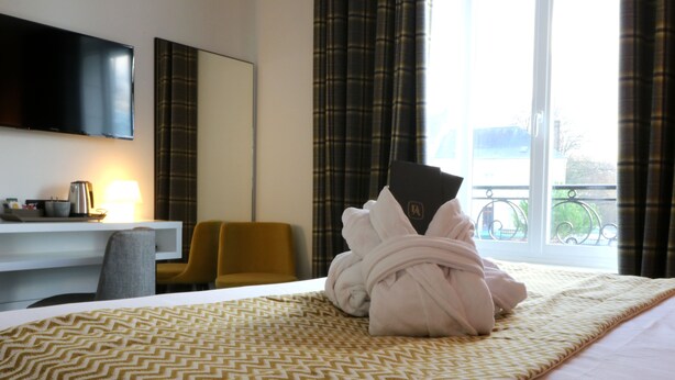 A hotel room with a bed, a desk, a chair, a TV, and a window with curtains. - Bel Ami (Pacy-sur-Eure)