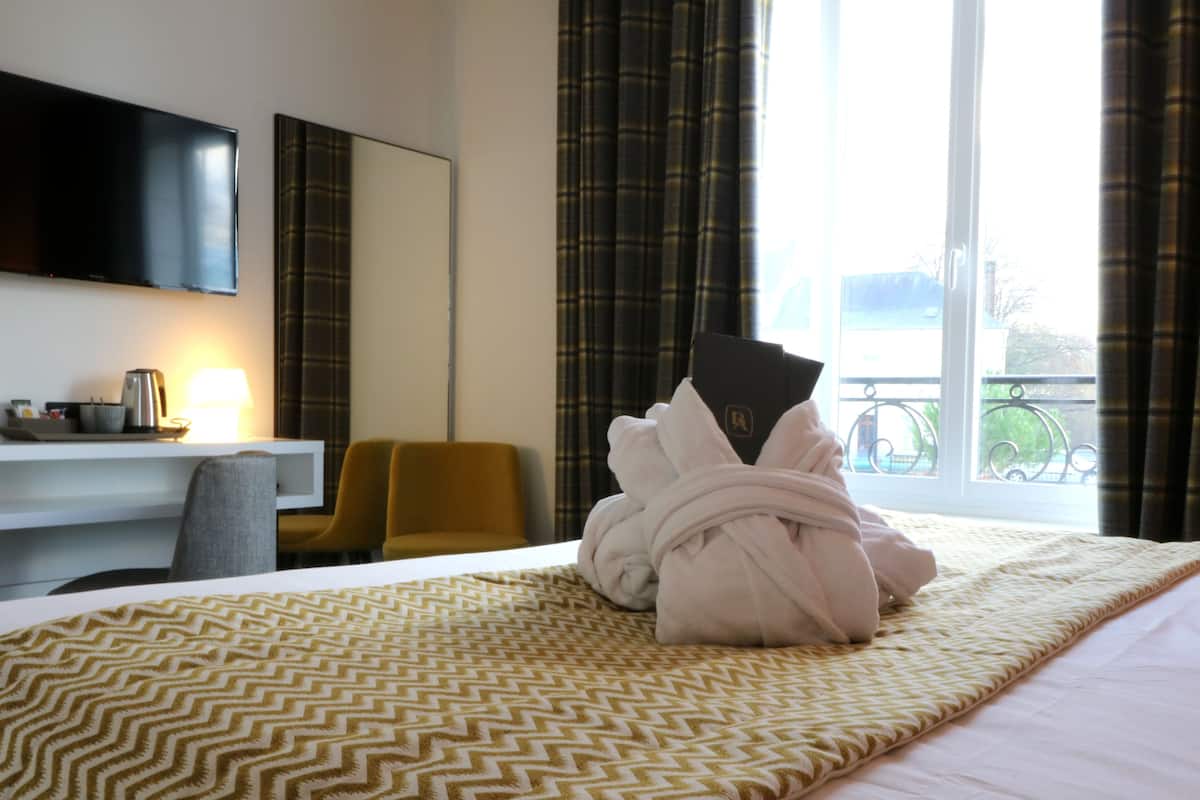 A hotel room with a bed, a desk, a chair, a TV, and a window with curtains.