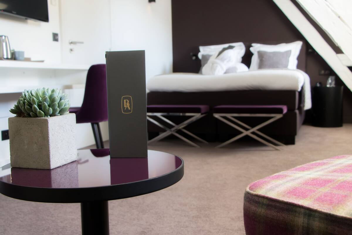 A modern hotel room with a bed, a desk, a chair, and a small potted plant.