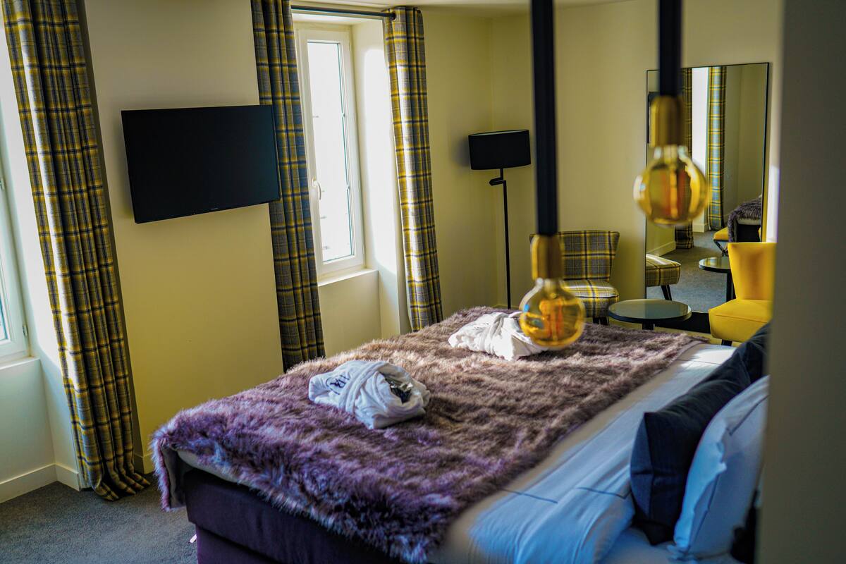 A hotel room with a bed, a flat-screen TV mounted on the wall, a lamp, and a mirror.