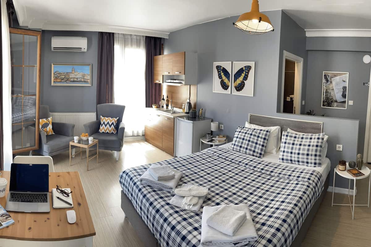 A hotel room with a bed, desk, chair, and a view of the cityscape through the window.