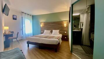 Une chambre d’hôtel avec un lit, un bureau, une chaise, une télévision et une salle de bain visible à travers une porte ouverte.