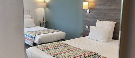 Habitación de hotel con dos camas, cabecera de madera, lámpara de noche y aplique de pared.
