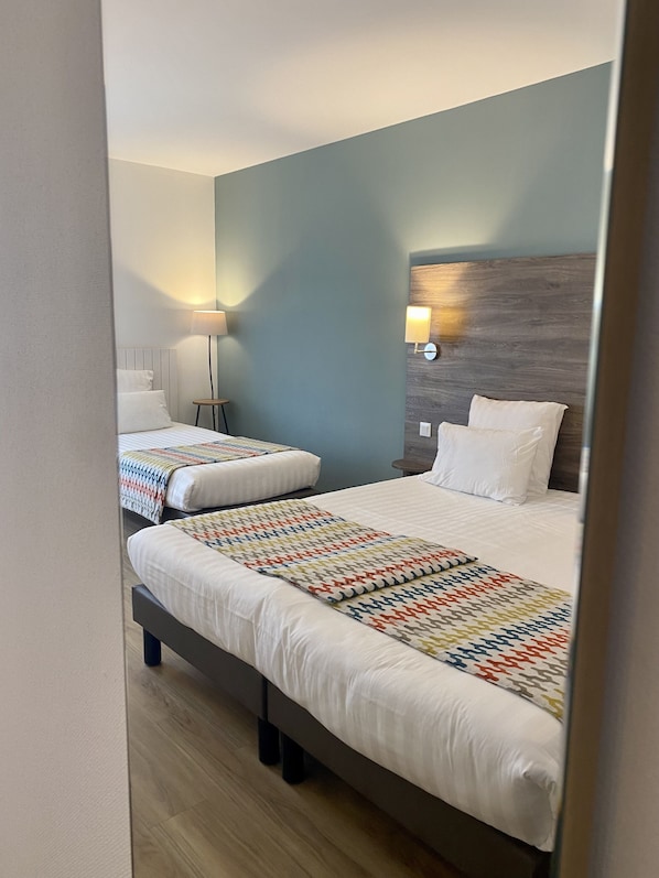 A hotel room with two beds, a wooden headboard, a bedside lamp, and a wall-mounted light fixture.