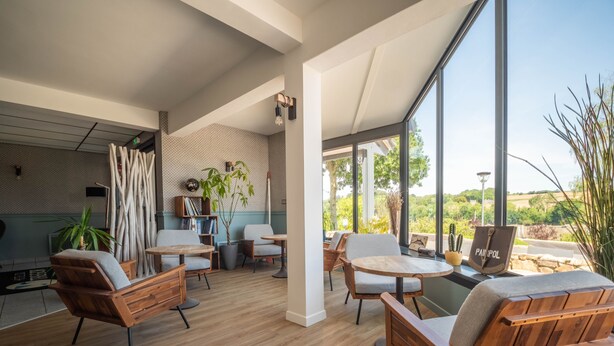 A modern interior with wooden flooring, a seating area with sofas and a table, a bookshelf, and a large window offering a view of greenery. - Hotel du Trégor (Treguier)