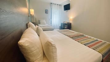 A hotel room with a bed, a desk, a chair, a TV, and a window with curtains.