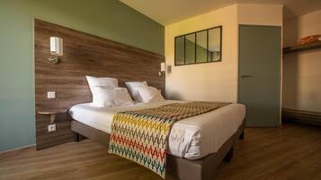 A neatly made bed in a room with a wooden headboard, a small bedside table, and a mirror on the wall.
