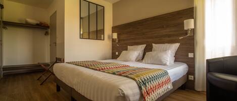 A hotel room with a large bed, a wooden headboard, a mirror, a bedside lamp, a chair, and a wooden floor.