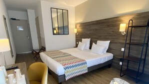 A hotel room with a bed, a chair, a table, a mirror, and a door. - Hotel du Trégor (Treguier)