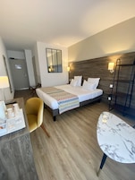 Una habitación de hotel con una cama, una silla, una mesa, un espejo y una puerta.