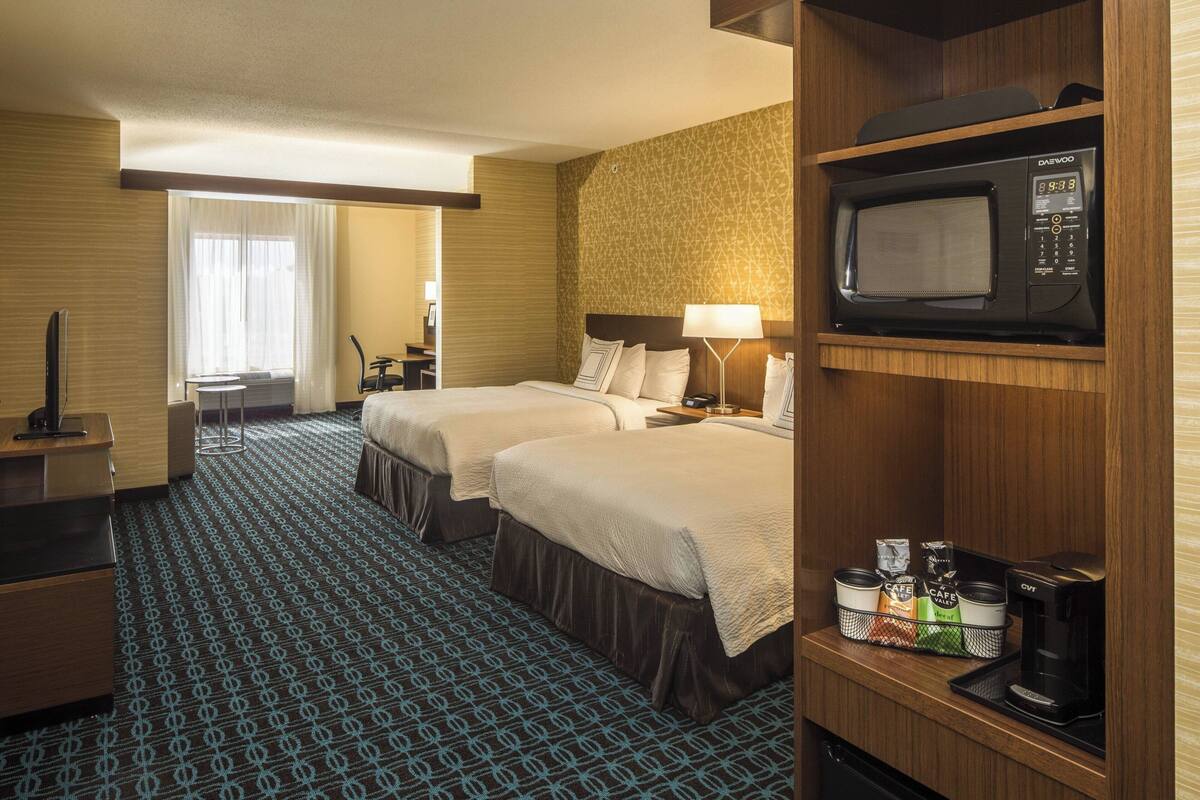 Habitación de hotel con dos camas, microondas, cafetera y minibar.