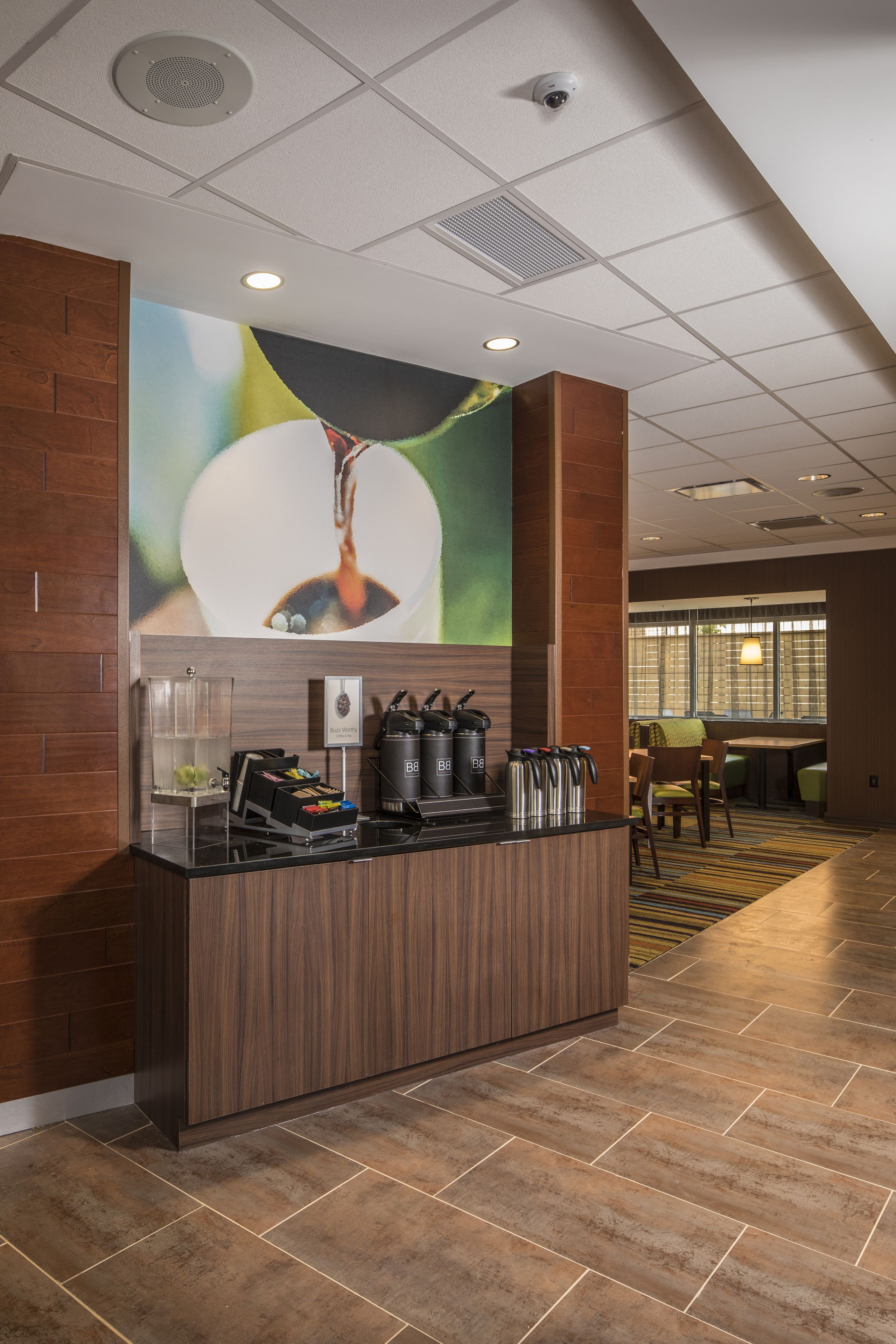 Uma área de recepção de hotel com balcão de madeira, cantinho de café e espaço de estar com vista para o exterior.
