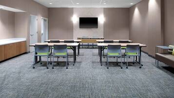 A conference room with a large table, chairs, a TV screen, and a carpeted floor.