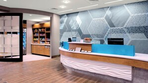 A modern reception area with a curved counter, a display of amenities, and a hexagonal patterned wall. - SpringHill Suites by Marriott Kansas City Lenexa City Center (Lenexa)