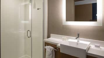 A modern bathroom with a glass-enclosed shower, a white sink with a mirror above it, and a towel hanging on a towel rack.