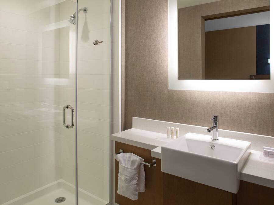 A modern bathroom with a glass-enclosed shower, a white sink with a mirror above it, and a towel hanging on a towel rack.