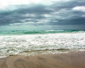 A beach with waves crashing onto the shore under a cloudy sky.