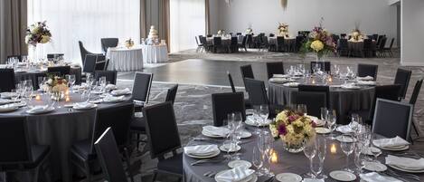 A banquet hall with round tables set for dining, featuring white tablecloths, black chairs, and floral centerpieces.