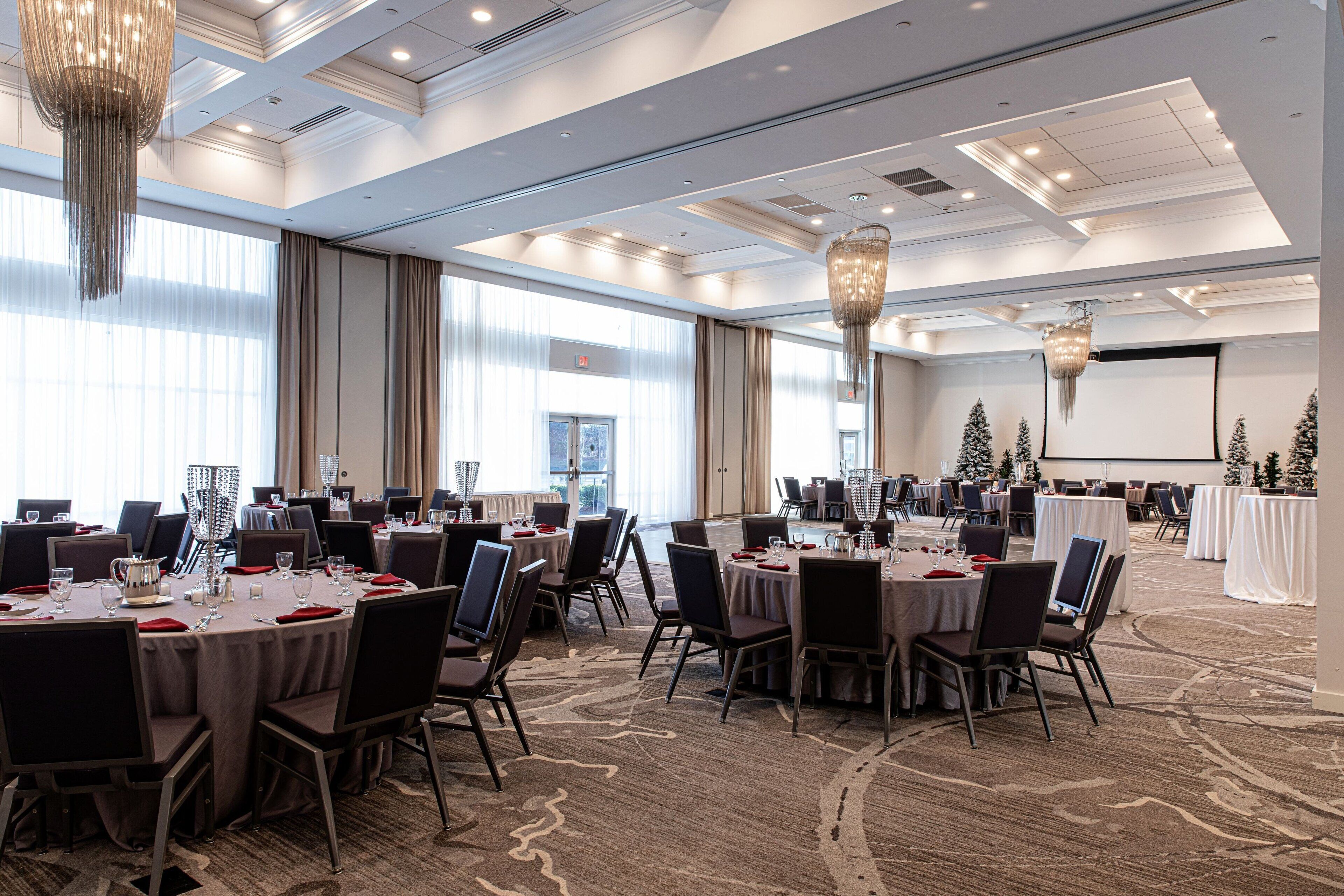 A spacious conference room with multiple tables and chairs, large windows, and decorative chandeliers.