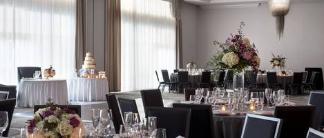 A banquet hall with round tables set for a formal event, featuring a tiered cake and floral centerpieces.