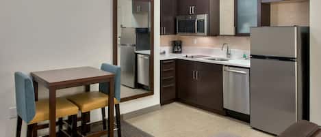 A compact kitchen with a dining area, including a table with two chairs, a microwave, a refrigerator, and a dishwasher.